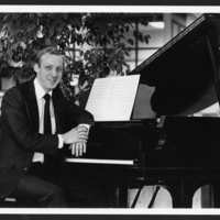 Robert Avalon at the piano, turning to face the camera, in suit and tie